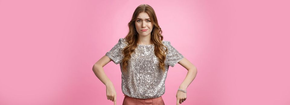 Well unimpressive. Girl gringe smirking frowning disappointment pointing down expressing displeased dislike, show bad uninteresting worthless product, being unamazed, standing pink background.