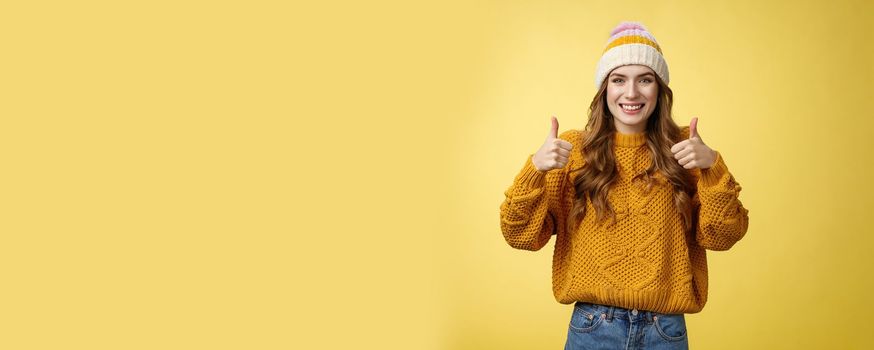 Supportive attractive 20s girl likes your idea show thumbs up positive reply affirmative answer standing pleased smiling recommending promotion satisfied give approval, agree yellow background.