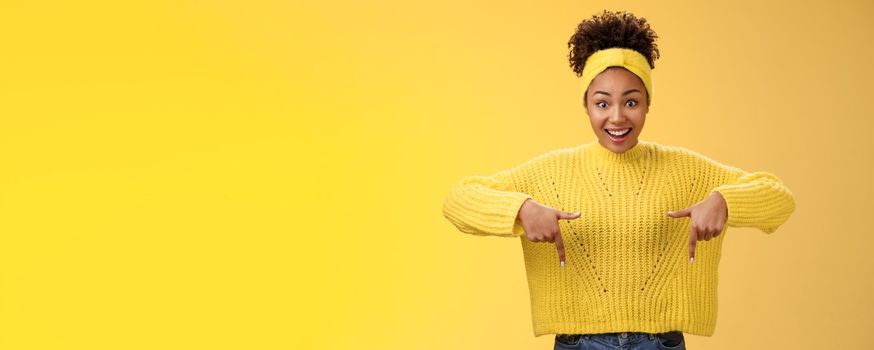 Enthusiastic impressed surprised beautiful african-american woman widen eyes drop jaw smiling gasping astonished pointing down amused standing yellow background showing amazing opportunity.