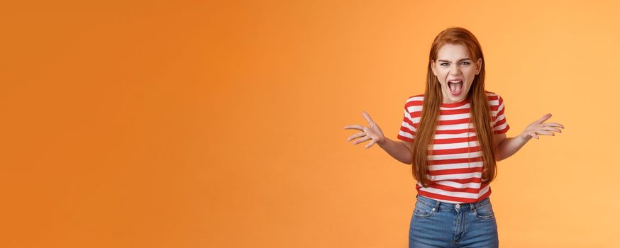 Pissed angry and annoyed redhead female arguing yelling with hatred and anger, spread hands sideways dismay, complain look disappointed upset and hateful, stand orange background. Copy space