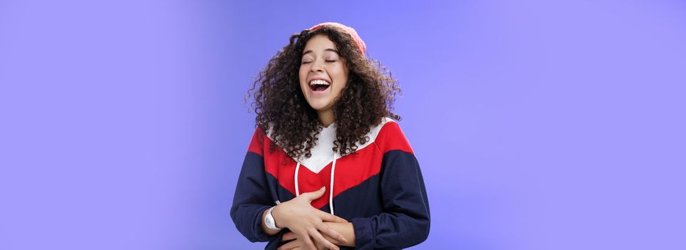 Girl hearing hilarious funny joke, making prank over friend laughing out loud feeling pain in belly as giggling too much holding hands on stomach close eyes and tilting back from joy and amusement.