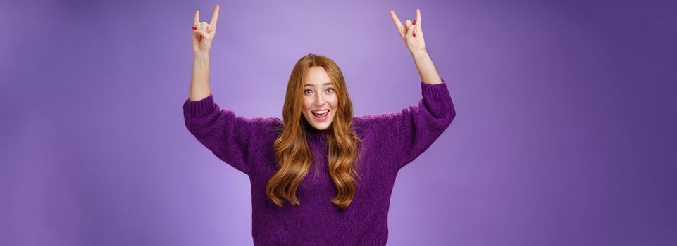 Girl feeling excited finally receiving tickets for favorite band show, raising hands with rock-n-roll gesture yelling yeah and smiling broadly, happy and thrilled against purple background. Copy space