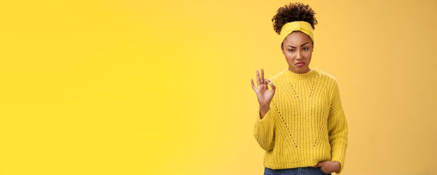 Well not bad. Portrait serious-looking confident arrogant young african-american woman agree effort good show okay ok normal gesture smug approval, standing yellow background impressed. Copy space