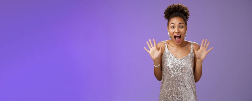 Shocked excited charming african-american woman in silver glittering dress raise palms amused screaming thrilled wondered widen eyes receive awesome incredible surprise, blue background.
