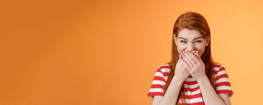 haha very funny. Silly tender cheerful redhead girl laughing, giggle hilarious joke, cover mouth press palms lips chuckling silent, mocking friend, stand upbeat orange background. Copy space