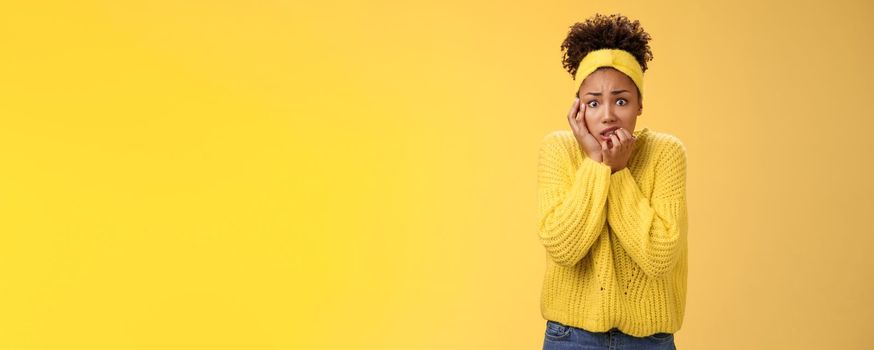 Afraid concerned nervous young african american female employee worried anxious be fired clench teeth stooping touch face insecure bit fingers standing scared terrified, yellow background.