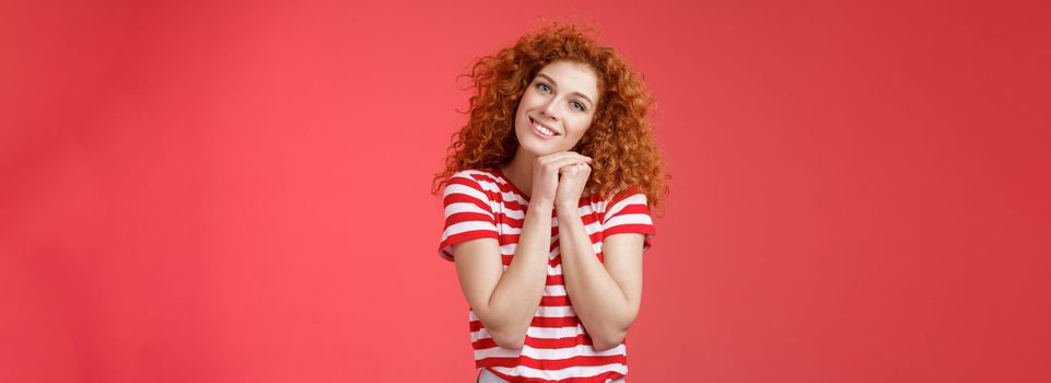 Lifestyle. Tender feminine caring redhead curly-haired female romantic gaze camera tilt head clench palms near head silly lovely look smiling delighted cheerful dreamy sighing look with sympathy.