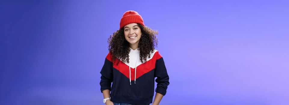 Girl invites join her team to srow snowballs. Portrait of friendly-looking carefree joyful woman with curly hair in red cute beanie and warm sweatshirt smiling joyfully getting ready for winter. Emotions, weather and fashion concept