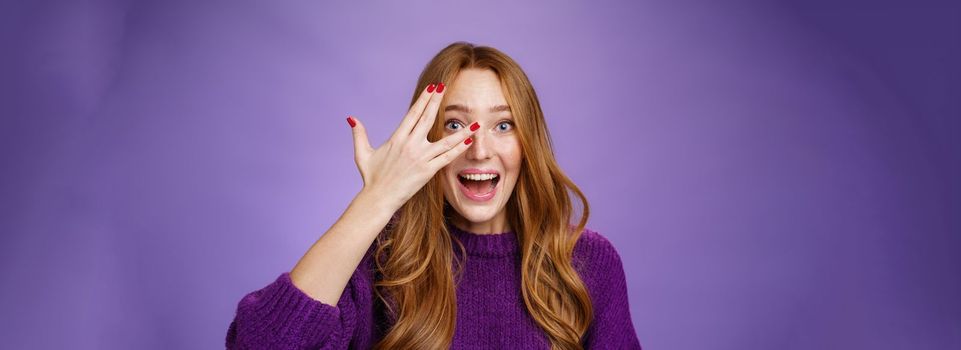 Waist-up shot of enthusiastic and charismatic cute funny redhead woman in purple sweater with cool nails showing peeking through holes in fingers and smiling optimistic and excited, looking surprised.