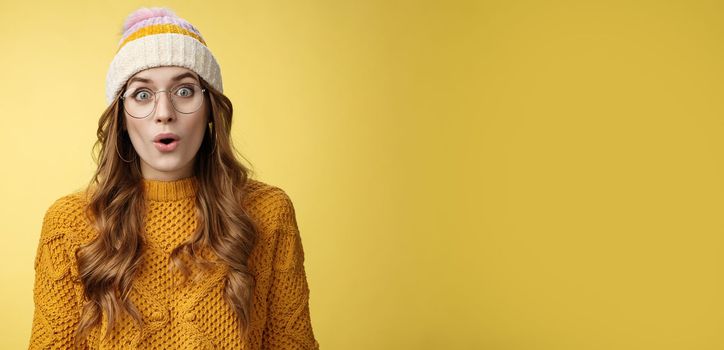 Surprised amazed charismatic good-looking young female student widen eyes wondered say wow amazed standing shocked impressed yellow background, wearing nerd glasses hat sweater.
