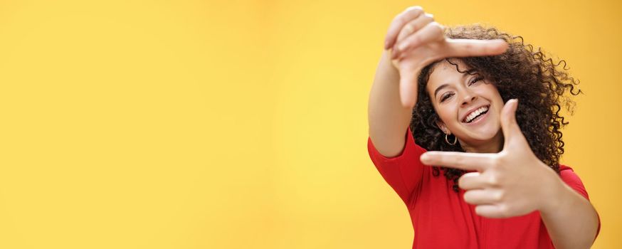 Lifestyle. Portrait of optimistic happy and creative female student imaging her new apartment as extending hands and showing frames gesture smiling through it at camera amused and carefree over yellow wall.