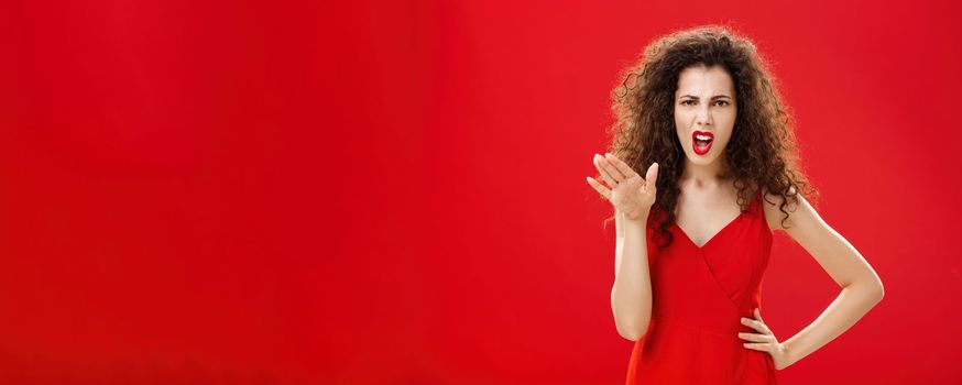 Girl chowing her temper to employees. being fed up with unappropriate behaviour complaining standing pissed and dissatisfied gesturing with palm and holding hand on hip over red background.