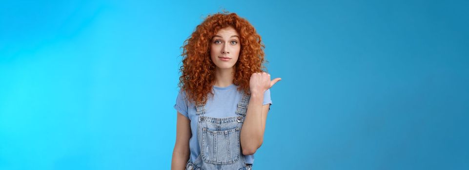 Lifestyle. Silly young happy cute redhead woman curly hairstyle smirking rate fine place hang out pointing left thumb introduce not bad choice asking out friend sit nearby cafe standing blue background.