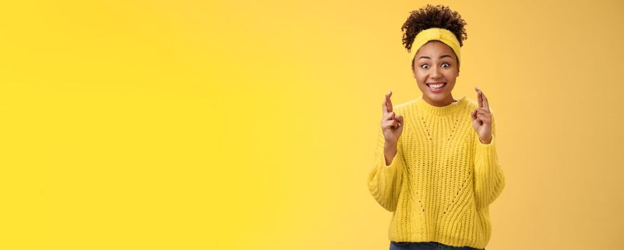 Excited optimistic hopeful young timid african-american girl. in yellow sweater smiling broadly thrilled anticipating good news bealive fortune cross fingers good luck grinning expect good news.