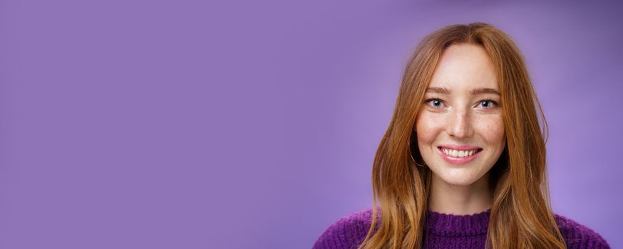 Headshot of charming attractive and happy young redhead woman with freckles and bright white smile, grinning satisfied at camera as posing over purple background friendly and delighted.