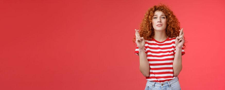 Lifestyle. Nervous young silly timid cute redhead ginger girl anticipating hopeful results believe praying squinting intense worry to win cross fingers good luck wish come true red background.