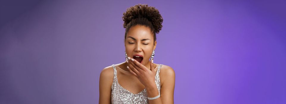 Tired attractive african-american party girl. had fun night yawning sleepy close eyes cover opened mouth tired standing exhausted in silver trendy dress wake up early standing blue background.