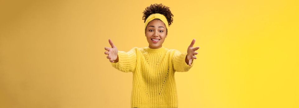 Come closer let me hug you. Touched lovely glad african-american young pretty woman extend arms wanna hold charming cute baby arms asking cuddle embrace friendly, posing yellow background.