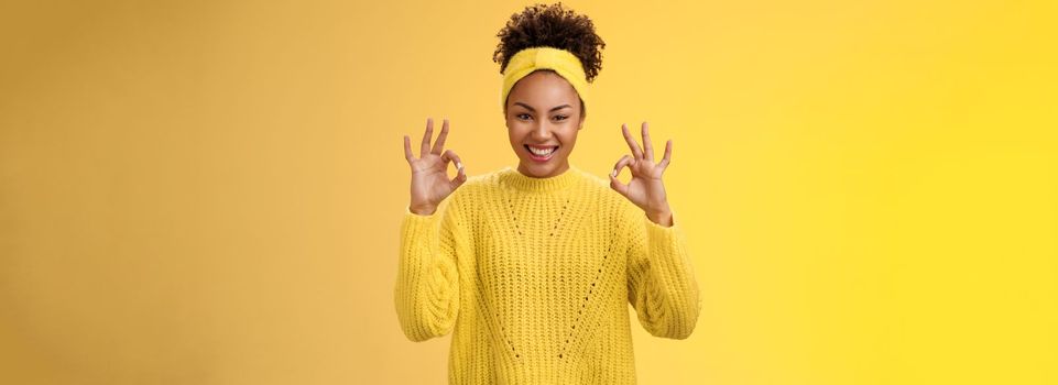 Count it done. Assured confident african-american woman in sweater headband show okay ok no worries gesture smiling self-assured plan goes fine, pleased good results, cheering yellow background.