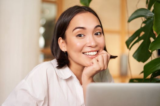 Beautiful young woman with happy smile, sitting in cafe with laptop, studying remotely, working online from distance. People and technology