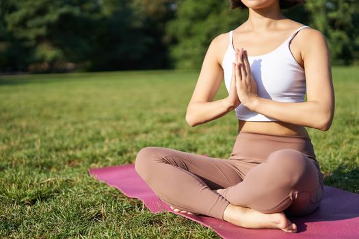 Woman meditating on lawn in park, sitting on sports mat, relaxing, breathing fresh air.