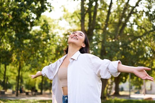 Portrait of carefree young asian woman dancing in park alone, enjoying freedom, smiling with joy. Copy space