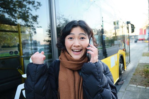 Happy asian girl talks on mobile phone and looks surprised, amazed by great news, achieve goal, hear something exciting.