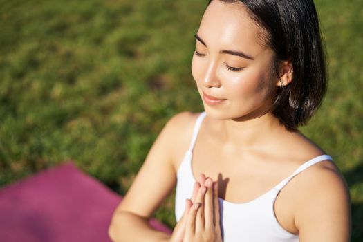 Portrait of young mindful woman, practice yoga, exercising, inhale and exhale on fresh air in park, sitting on rubber mat.