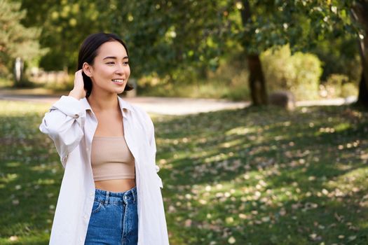 Beautiful young asian girl smiling, laughing and walking along park, enjoying summer sunny day. People and lifestyle concept