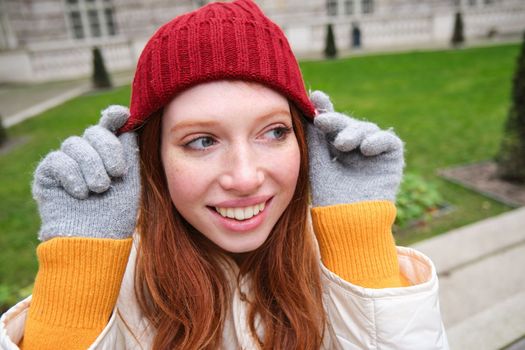 Cute girl student in red hat, warm gloves, sits in park, smiles and looks happy. Copy space