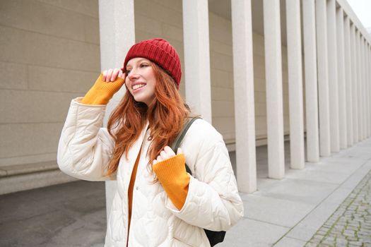 Female tourist in red hat with backpack, sightseeing, explores historical landmarks on her trip around europe, smiling and posing on street.