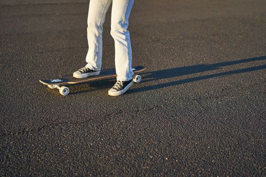 Cropped shot of legs on longboard. Skater girl riding her skateboard on street. Female teenager on cruiser.