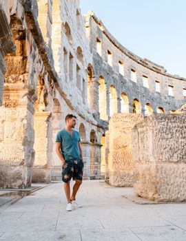 Young men tourists visit Pula city in Croatia, Roman Amphi theatre Arena in Pula on a bright summer day evening, A wall fragment of ancient Roman amphitheater Coliseum PulaPula, Croatia. 