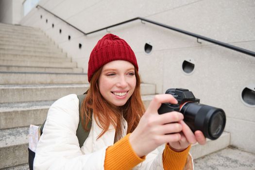 Urban people and lifestyle. Happy redhead woman takes photos, holding professional digital camera, photographing on streets.