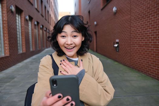 Portrait of amazed girl, looks at smartphone screen and gasps from happiness, reads good news on text message, being impressed by smth on mobile phone.