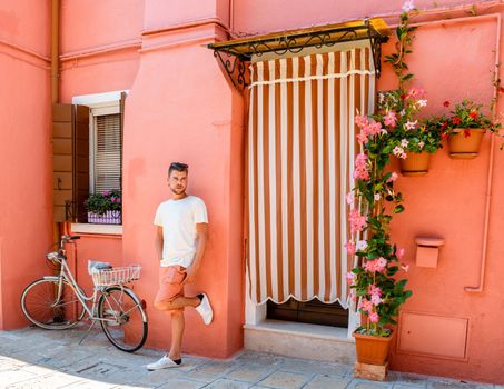 Young men standing against a pink wall at the colorful streets of the village Burano Venice Italy colorful canal whit boats and vibrant houses. 
