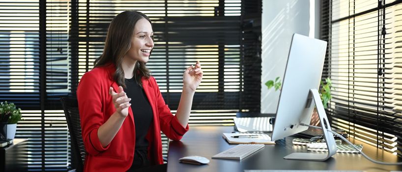 Side view of caucasian woman corporate CEO in red luxury suit watching online webinar on computer in modern office.