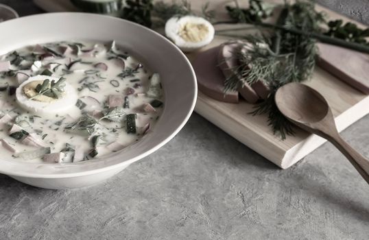 Traditional Russian cold summer soup - okroshka with fresh vegetables, sausage and kefir. Composition with traditional dishes and spices. View from above.