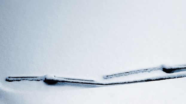 Snowy windshield on a car with wipers. Winter concept for traffic and road safety.