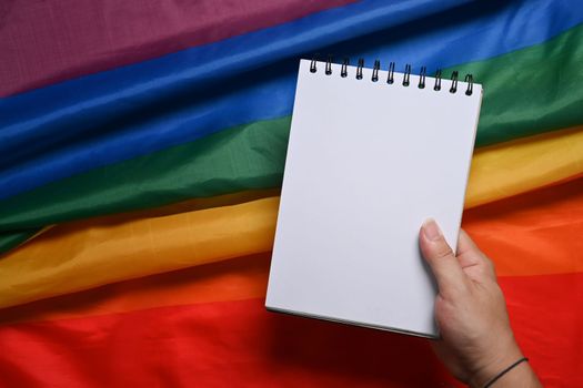 Hand of man holding empty notebook over rainbow flag.