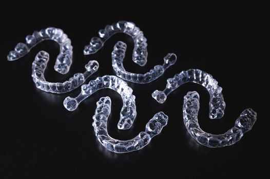 A pattern of transparent aligners, invisible braces lies on a black background. No people.
