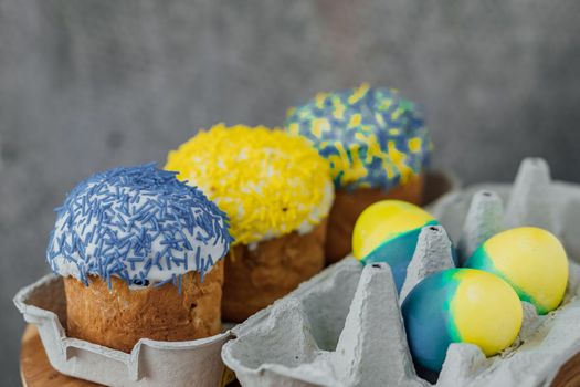 Easter cakes in the colors of the flag of Ukraine, yellow and blue in a cardboard stand with eggs, Easter eggs. place for text. selective focus.