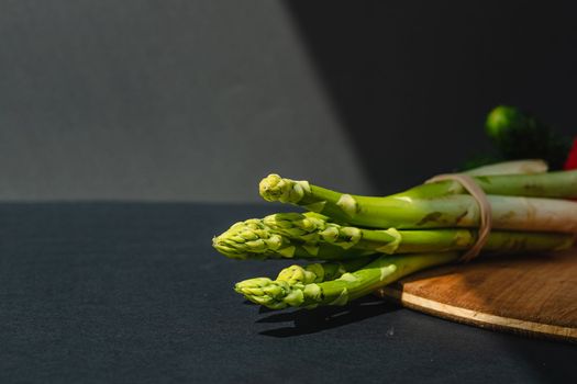 branches of fresh green asparagus on a wooden board, dark gray background, top view. Basic trend concept with copy space