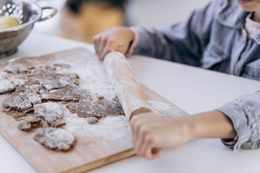 Little girl's hand making traditional Christmas cookies. Raw dough and cutters for the holiday cookies on a dark table. Preparing Christmas gingerbread men.