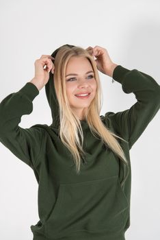 Stylish beautiful young blond woman in a green tracksuit poses near a white wall in the room. Fitness lady