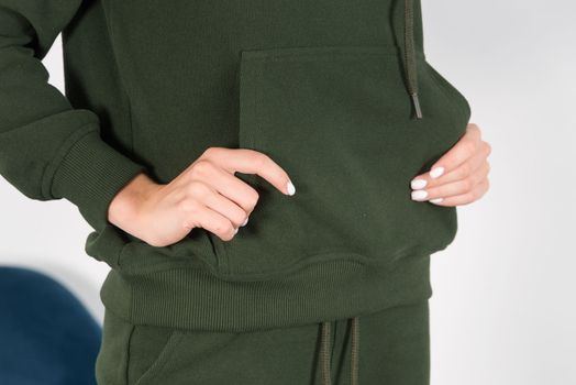 Stylish beautiful young blond woman in a green tracksuit poses near a white wall in the room. Fitness lady