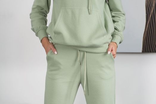 Stylish beautiful young blond woman in a green tracksuit poses near a white wall in the room. Fitness lady