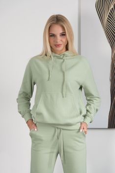 Stylish beautiful young blond woman in a green tracksuit poses near a white wall in the room. Fitness lady