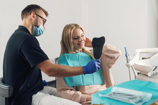 Portrait of a dentist in eyeglasses who treats teeth of young blond woman patient.