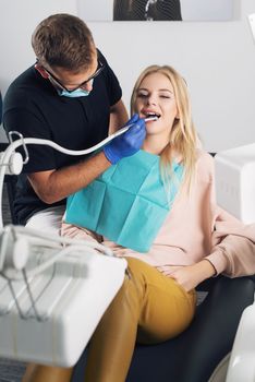 Portrait of a dentist in eyeglasses who treats teeth of young blond woman patient.